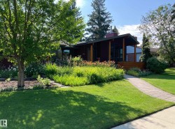 The property features a well-maintained lawn, mature trees, and a landscaped front garden with various plants and flowers - 