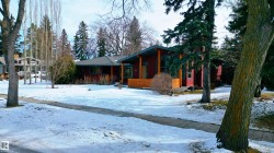 The property features a modern ranch-style home with a dark red exterior, a gray roof, and a wooden porch - 