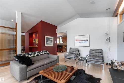 Living area featuring light hardwood flooring, high ceilings, a fireplace with stacked wood, and a striking accent wall - 9715 141 Street Nw, Edmonton, AB - Indoor Photo Showing Living Room