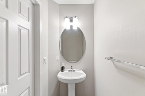 Bathroom featuring a pedestal sink, an oval mirror, and a wall-mounted light fixture - 1668 Chapman Way, Edmonton, AB - Indoor Photo Showing Bathroom