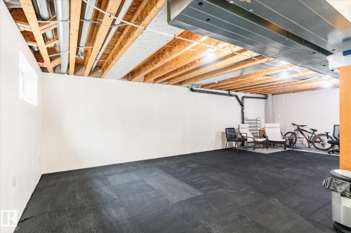 Basement area featuring white walls, an exposed wooden beam ceiling with visible ductwork, and black interlocking floor tiles - 1668 Chapman Way, Edmonton, AB - Indoor Photo Showing Basement