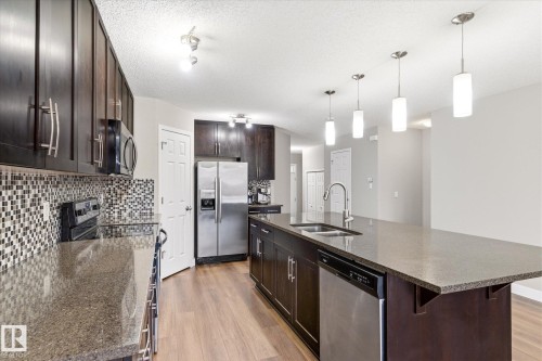 The kitchen features dark wood cabinetry, stainless steel appliances, a mosaic tile backsplash, and a large island with a double sink and pendant lighting - 1668 Chapman Way, Edmonton, AB - Indoor Photo Showing Kitchen With Double Sink With Upgraded Kitchen