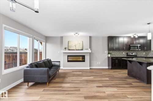 Open concept living space featuring wide plank flooring, large windows, a fireplace, and a kitchen with dark cabinetry and a tiled backsplash - 1668 Chapman Way, Edmonton, AB - Indoor With Fireplace