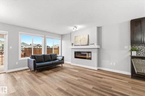 The property features a bright living area with light wood-style flooring, large windows, and a contemporary fireplace integrated into the wall - 1668 Chapman Way, Edmonton, AB - Indoor Photo Showing Living Room With Fireplace