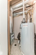 Utility area featuring a water heater, furnace, exposed ductwork, and tile flooring - 