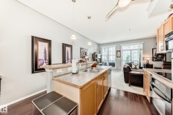 This inviting open-concept living area features rich hardwood flooring, a kitchen island with a double basin sink, and ample natural light from large windows - 