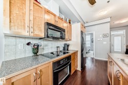 The kitchen features light wood cabinetry, a built-in microwave, an electric cooktop with an oven, and a black refrigerator - 