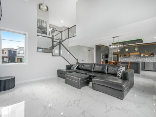 This property features white tiled flooring, a modern staircase with glass panels, and a sleek kitchen with dark cabinetry and stainless steel appliances - 1104 152 Avenue, Edmonton, AB - Indoor