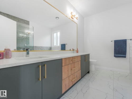 Spacious bathroom featuring a large vanity with stone countertops, a gold-framed mirror, and sleek gray and wood-toned cabinetry with gold hardware - 1104 152 Avenue, Edmonton, AB - Indoor Photo Showing Bathroom