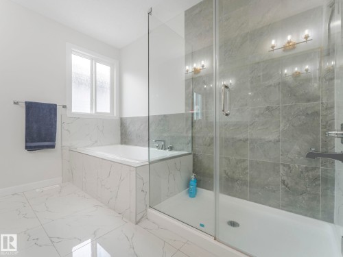 The bathroom features white tile flooring with gray veining, a built-in bathtub with a white tiled surround, and a clear glass shower enclosure with gray tiled walls - 1104 152 Avenue, Edmonton, AB - Indoor Photo Showing Bathroom