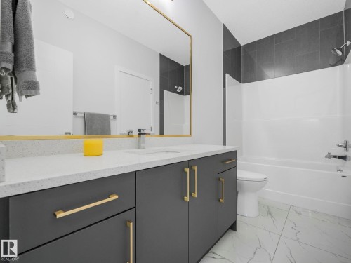 Bathroom featuring a vanity with a white countertop and dark grey cabinetry with gold-toned hardware, a full-width mirror with a gold-toned frame, and a white bathtub with dark grey tiled surround - 1104 152 Avenue, Edmonton, AB - Indoor Photo Showing Bathroom