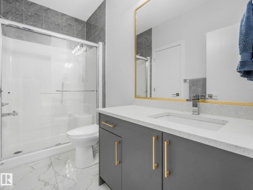 This bathroom features a contemporary gray vanity with gold-toned hardware, a white countertop with an integrated sink, and a large mirror with a gold-toned frame - 1104 152 Avenue, Edmonton, AB - Indoor Photo Showing Bathroom