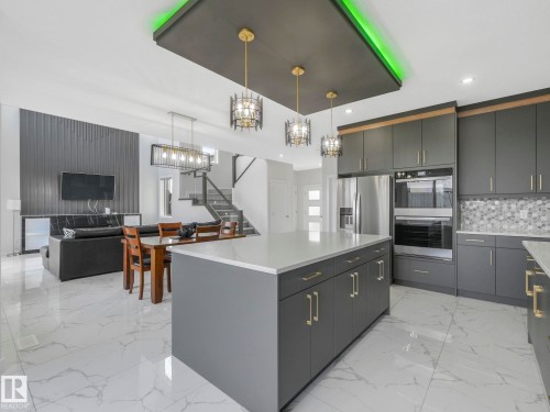 Modern kitchen featuring a large center island with a light-colored countertop, dark gray cabinetry with gold-toned hardware, and a tile backsplash - 1104 152 Avenue, Edmonton, AB - Indoor Photo Showing Kitchen With Upgraded Kitchen
