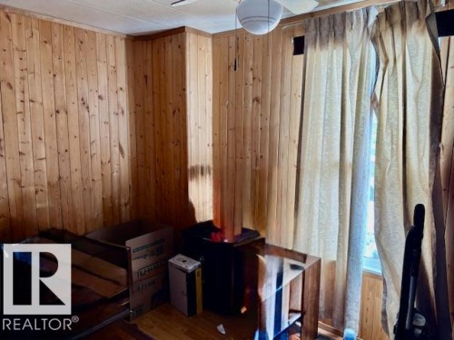 This room features wood paneling on the walls, a ceiling fan with an integrated light fixture, and a window with curtains - 4809 53 Ave, Willingdon, AB - Indoor Photo Showing Other Room