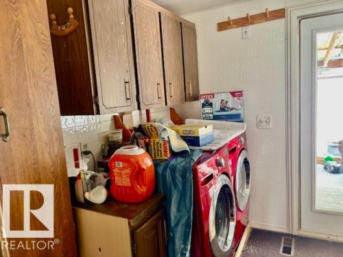 The utility area features wooden cabinetry, a white tiled backsplash, and a white paneled wall with a wooden coat rack - 4809 53 Ave, Willingdon, AB - Indoor Photo Showing Laundry Room