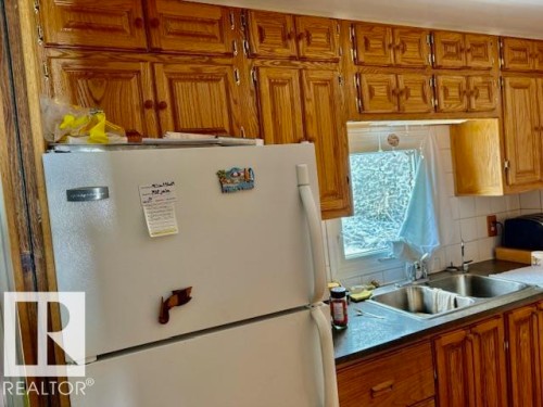 Kitchen featuring wood cabinetry, a white refrigerator, and a double basin sink - 4809 53 Ave, Willingdon, AB - Indoor Photo Showing Kitchen With Double Sink