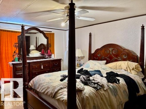 This bedroom features a ceiling fan, light-colored walls, and a window with orange curtains - 4809 53 Ave, Willingdon, AB - Indoor Photo Showing Bedroom