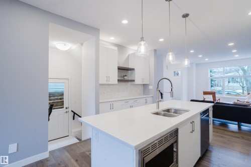 Modern kitchen featuring white cabinetry, a large kitchen island with a double basin sink and a stainless steel microwave, and recessed lighting - 9612 72 Avenue, Edmonton, AB - Indoor Photo Showing Kitchen With Double Sink With Upgraded Kitchen
