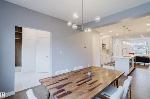 Dining area featuring a modern chandelier, a wooden table, and hardwood flooring, with a partial view of the kitchen and living area - 9612 72 Avenue, Edmonton, AB - Indoor