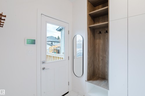 Entryway featuring a white door with a window pane, a built-in storage unit with wood-grain shelves and white cabinetry, and a full-length oval mirror - 9612 72 Avenue, Edmonton, AB - Indoor Photo Showing Other Room