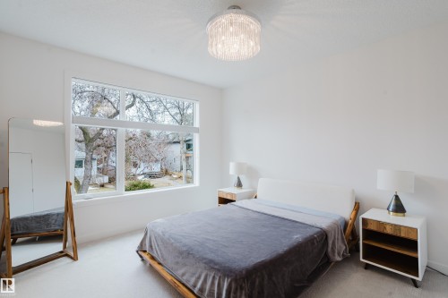 The bedroom features a large window, a modern ceiling light fixture, and two nightstands with built-in shelving - 9612 72 Avenue, Edmonton, AB - Indoor Photo Showing Bedroom