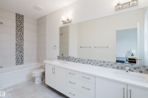 Well-appointed bathroom featuring a spacious vanity with two sinks, a full-width mirror, and a combination bathtub and shower with distinctive tile work - 9612 72 Avenue, Edmonton, AB - Indoor Photo Showing Bathroom