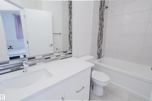 The bathroom features a vanity with a white countertop and an integrated sink, a rectangular mirror with a mosaic tile accent, a toilet, and a bathtub with a shower - 9612 72 Avenue, Edmonton, AB - Indoor Photo Showing Bathroom