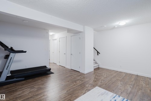 Spacious room featuring hardwood flooring, white walls, and a staircase with a black handrail - 9612 72 Avenue, Edmonton, AB - Indoor Photo Showing Gym Room