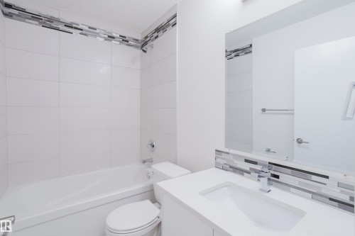 Contemporary bathroom featuring a white tile shower surround with decorative mosaic accent tiles, a white vanity with an integrated sink, and a large mirror - 9612 72 Avenue, Edmonton, AB - Indoor Photo Showing Bathroom