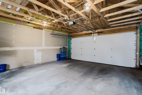 The property includes a spacious garage with exposed wooden ceiling trusses, a concrete floor, and a large white overhead garage door - 9612 72 Avenue, Edmonton, AB - Indoor Photo Showing Garage