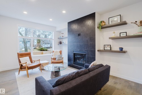 The living area features hardwood floors, a modern fireplace with a dark tiled surround, and large windows providing natural light - 9612 72 Avenue, Edmonton, AB - Indoor Photo Showing Living Room With Fireplace