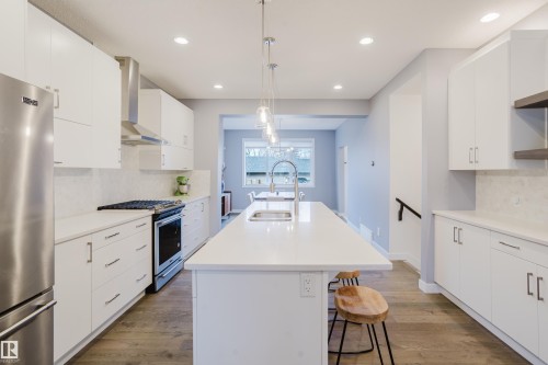 The kitchen features white cabinetry, stainless steel appliances, and an island with a sink and pendant lighting - 9612 72 Avenue, Edmonton, AB - Indoor Photo Showing Kitchen With Double Sink With Upgraded Kitchen