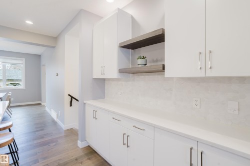 This versatile space features white cabinetry with brushed nickel hardware, open shelving, and a light-colored countertop with a matching backsplash - 9612 72 Avenue, Edmonton, AB - Indoor