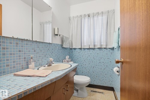 Bathroom featuring a wood vanity with a tiled countertop and an integrated sink, a large mirror, and tiled walls - 9131 74 Street, Edmonton, AB - Indoor Photo Showing Bathroom