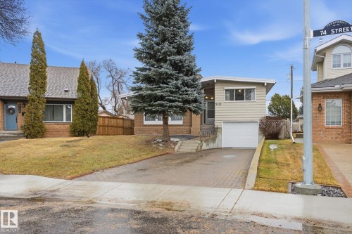 The property features a front yard with a lawn, mature evergreen trees, and an attached garage with a white door - 9131 74 Street, Edmonton, AB - Outdoor With Facade