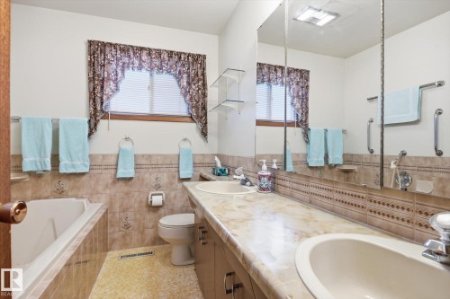 The bathroom features a double vanity with two sinks, a bathtub, and a window with blinds - 9131 74 Street, Edmonton, AB - Indoor Photo Showing Bathroom