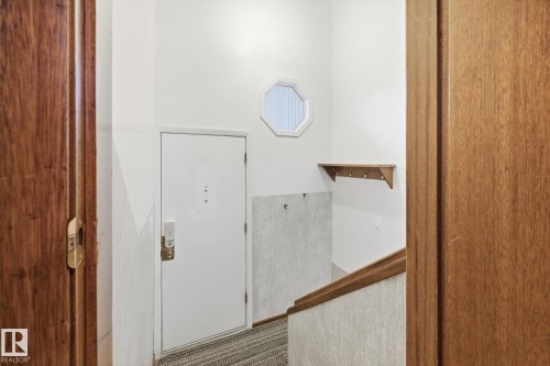 Entryway featuring a white door, an octagonal window, a wooden shelf with hooks, and a wooden handrail - 9131 74 Street, Edmonton, AB - Indoor Photo Showing Other Room