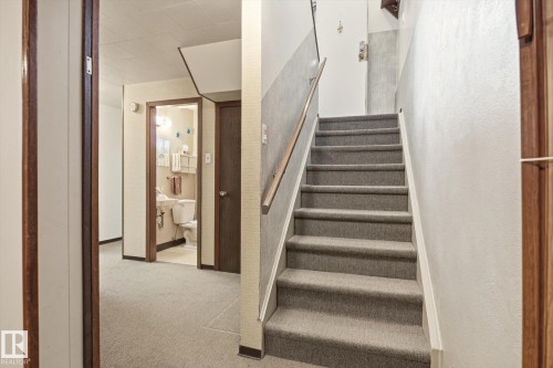 Carpeted staircase with a wooden handrail, featuring neutral wall finishes - 9131 74 Street, Edmonton, AB - Indoor Photo Showing Other Room