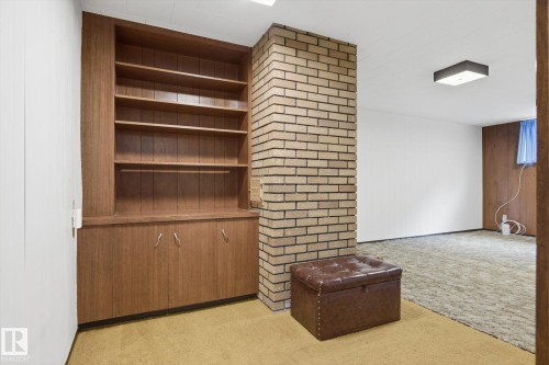 This area features a built-in wooden shelving unit with cabinets, a brick-faced column, and carpeted flooring - 9131 74 Street, Edmonton, AB - Indoor Photo Showing Other Room