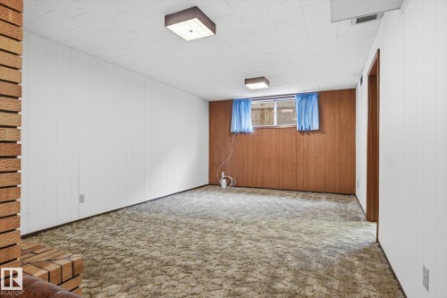 This spacious room features a window with blue curtains, wood paneling, and an exposed brick accent wall - 9131 74 Street, Edmonton, AB - Indoor Photo Showing Other Room