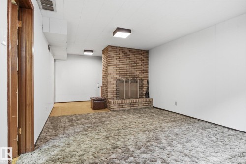 The property features a spacious room with a brick fireplace, a metal fire screen, and a textured carpet - 9131 74 Street, Edmonton, AB - Indoor Photo Showing Other Room