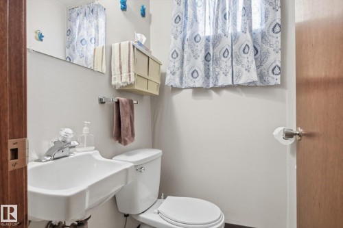The bathroom features a white sink with a chrome faucet, a white toilet, and a window with patterned curtains - 9131 74 Street, Edmonton, AB - Indoor Photo Showing Bathroom