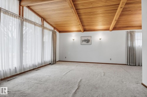 This room features a vaulted wood ceiling with exposed beams, large windows providing natural light, white walls, and wall-mounted sconces - 9131 74 Street, Edmonton, AB - Indoor Photo Showing Other Room