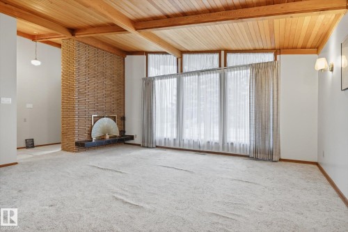 The spacious living area features a brick fireplace with a dark hearth, a wooden beamed ceiling, and large windows with sheer curtains - 9131 74 Street, Edmonton, AB - Indoor Photo Showing Other Room