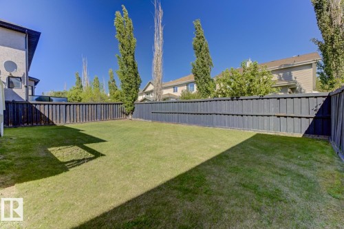The property features an extensive grassy yard with a dark-toned privacy fence - 3105 Tredger Place, Edmonton, AB - Outdoor With Backyard