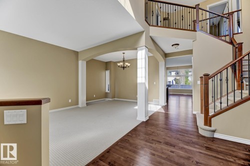 This interior view features a grand staircase with dark wood railings and black metal spindles, leading to an upper level - 3105 Tredger Place, Edmonton, AB - Indoor Photo Showing Other Room