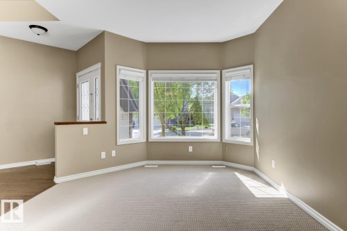 This bright interior space features bay windows, neutral-toned walls, and a combination of carpet and hardwood flooring - 3105 Tredger Place, Edmonton, AB - Indoor Photo Showing Other Room