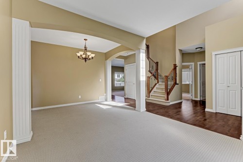 Living area featuring light-colored carpeting and a chandelier, with a staircase showcasing wooden railings and white risers, and dark wood flooring in the entryway - 3105 Tredger Place, Edmonton, AB - Indoor