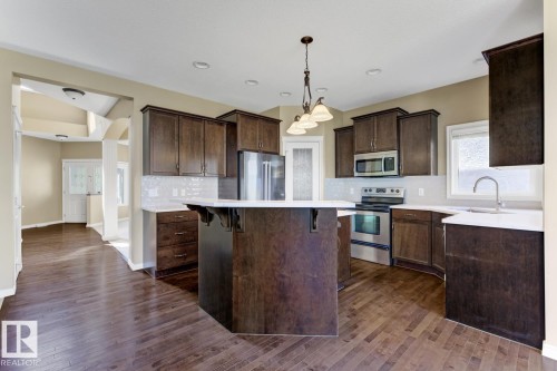 Well-appointed kitchen featuring dark wood cabinetry, stainless steel appliances, a center island with a light-colored Quartz countertop, and a window above the sink - 3105 Tredger Place, Edmonton, AB - Indoor Photo Showing Kitchen With Stainless Steel Kitchen With Upgraded Kitchen