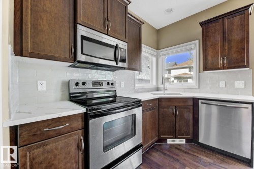 Kitchen featuring dark wood cabinetry, stainless steel appliances, white subway tile backsplash, and light-colored countertops - 3105 Tredger Place, Edmonton, AB - Indoor Photo Showing Kitchen With Stainless Steel Kitchen